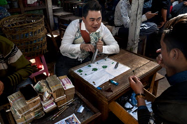 A jade seller (centre), sitting beside a huge pile of Kyat notes, polishes jade stones as he talks with a buyer (right) in the Mandalay Jade Market.