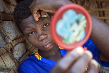 A Baaka (pygmy) girl uses a razor blade and a mirror to shave hairs from her forehead.
