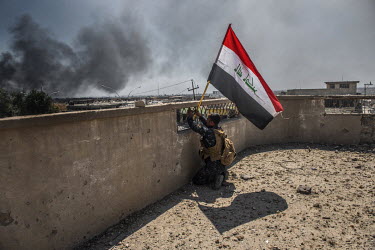 A federal policeman exposes himself to enemy fire as he raises the Iraqi flag on top of a building captured just hours earlier from ISIS militants during heavy fighting in the al Thawra neighbourhood...