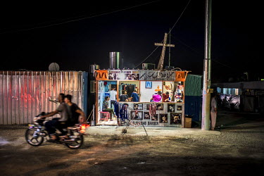 Two men ride a motorbike past a barber's shop inside an IDP camp in Erbil where thousands of Christians, displaced by the advance of ISIS, have found sanctuary.