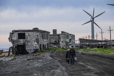 People walking past derelict buildings of the so-called 2nd Base, an area of Oktyabrskiy that is heavily affected by coastal erosion. Since the 1970s the sea has been claiming the land, destroying par...
