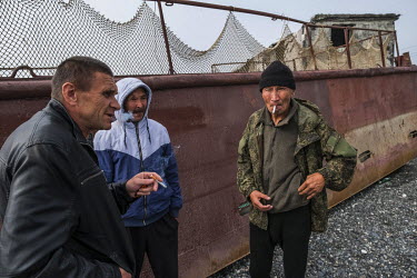 A group of men who come from the Republic of Buryatia to work at the town's fish factory 'Narody Severa', talking near a fish transport barge left on the beach. On stormy days the factory closes and m...