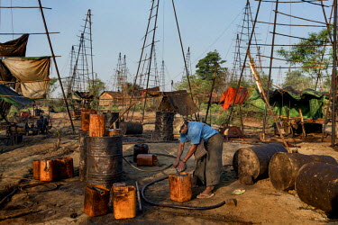 A man transfers oil into a bucket on Nga Naung Mone, Myanmar's largest unregulated oil field.