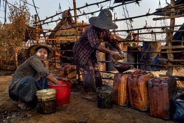 Women, who use rags to mop up and scavenge spilled oil, transfer it into buckets that they can sell for about 6000 Kyat (GBP 3.40) each, on Nga Naung Mone, Myanmar's largest unregulated oil field.