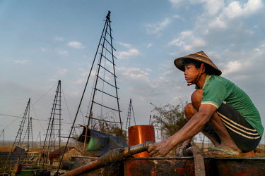 A man collecting oil from a wildcat prospector's drilling site in Nga Naung Mone, Myanmar's largest unregulated oil field, for transportation to a central collection point.