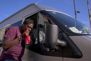 A man with a cup of Coca-Cola in his hand checks himself in a van's mirror.