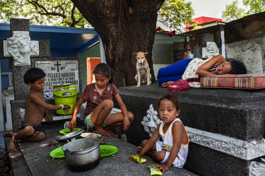 Three siblings eat lunch on tombs where they live in Manila North Cemetery. Manila North Cemetery is home to thousands of 'informal settlers' who have built shacks using in and around the mausoleums,...