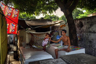 A man swings his grandchild in a cot suspended over tombs next to the shack he lives in at Manila North Cemetery.  Manila North Cemetery is home to thousands of 'informal settlers' who have built shac...