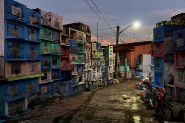 A woman checks her phone as she sits with her dog at dusk in Barangka Cemetery. Due to overcrowding many tombs are stacked on top of each other in Manila.