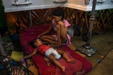 Julie Beth, nine, comforts her sister Erika, one year old, as they rest beneath the coffins of their brother Francis Manosca, five, (right) and their father Domingo Manosca, 44, at their wake. The fat...