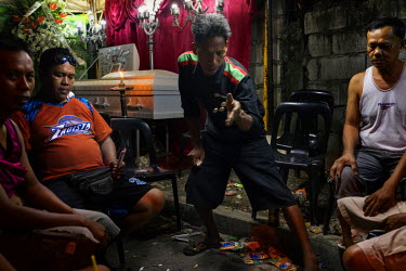 A man tosses coins while playing a gambling game to raise money for his funeral costs at the wake of Maricris Viloria, 34, a tricycle taxi driver who was killed in what appeared to be a drug-related e...