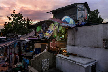 A man splits wood to cook dinner in a shanty home amongst graves in the Pasay Cemetery.