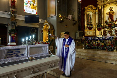 A priest sprinkles holy water on the coffin of Christian Mufable, 34, at a mass in San Roque Parish Church ahead of his interment in Sangangdaan Cemetery. Mufable was killed on 21 November 2016 during...