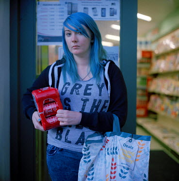 A woamn with dyed blue hair leaves a shop with a six-pack of Coca-Cola.