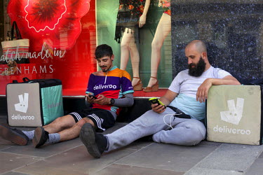 Deliveroo workers use their mobile phones while taking a break on the High Street.