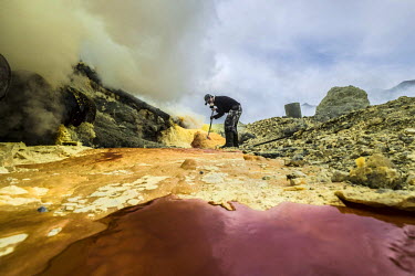 Miskadi, a 36 year old miner, uses a metal pole to brake off lumps of sulphur inside the Ijen crater. The sulphur is red when hot, turning yellow as it cools. More than 200 people come here daily to c...