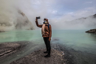 A tourist takes a selfie beside a lake of sulphuric acid in the Kawah Ijen crater. While many tourists visit to witness the natural phenomenon, more than 200 miners come daily to collect the sulphur w...