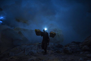 A sulpher miner carries his load past clouds of toxic gas before dawn in the Kawah Ijen crater. More than 200 people come here daily to collect sulphur, which occurs naturally in volcanic emissions. A...