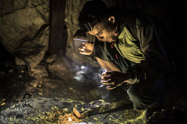 A sulphur miner plays around with sulphur chips, burning them to try and produce blue flames, as he takes a break from working in the Ijen crater. More than 200 people come here daily to collect sulph...
