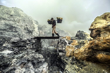An elderly miner Pa Bu, carries a load of sulphur over a bridge inside the crater of the Ijen volcano. More than 200 people come here daily to collect sulphur, which occurs naturally in volcanic emiss...