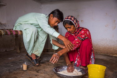 Daniel Ali (12) rolls up his mother's sleeves as she prepares dough for chapatis at her family bakery in Manhiala, Chakwal District. Kausar Shaheen suffers from cataracts in both eyes that severely re...