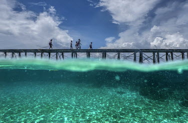 Bajau youths traverse a wooden walkway connecting Pulo Papan village with Malenge Island.