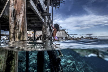 A young Bajau girl climbs up a wooden ladder into her home in the stilt village of Pulo Papan in the Togean Islands.