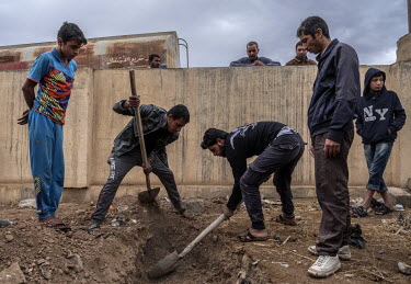 Bystanders look on as relatives of Mushal Fathi Mahmood, who died in an airstrike, dig up his corpse in western Mosul, in order to enable a DNA confirmation of his identity.