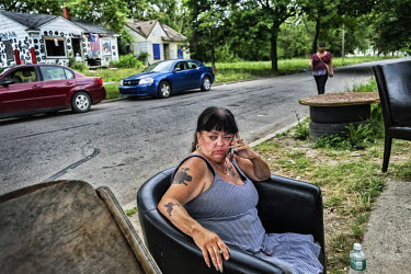 A woman sits on an armchair at the roadside using a mobile phone. The chairs are used as a meeting place for people in the neighbourhood.