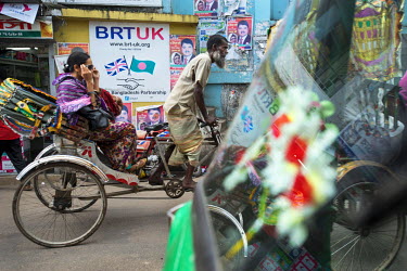 A woman in a rickshaw passes a sign advertising the British Bangladeshi Partnership, a UK registered charity.