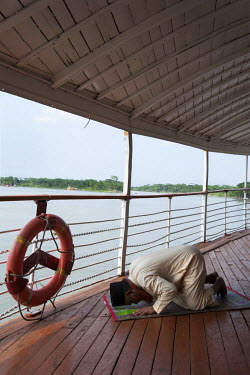 A Muslim passenger at prayer on the deck of the PS Mahsud during a voyage between Dhaka and Khulna.Built in a Scottish shipyard on the River Clyde in 1929 this was one of many boats used by the Britis...