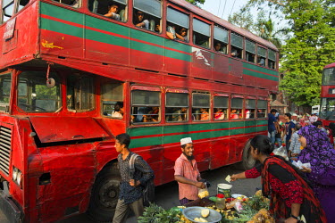 A food vendor selling pineapples at a bus stop where red and green double decker buses, painted in the colours of the Bangladeshi flag, collect students from the University of Dhaka at the end of the...