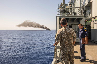 A Spanish officer (right) and a colleague from another European country, onboard the Spanish navy vessel the Cantabria, observe the plume of smoke produced by a burning rubber boat following the rescu...