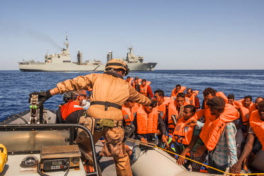A Spanish marine on a fast boat extends his hand to indicate to the occupants of a drifting boat, crowded with migrants, during a rescue operation on the Mediterranean Sea. In the background is the mo...