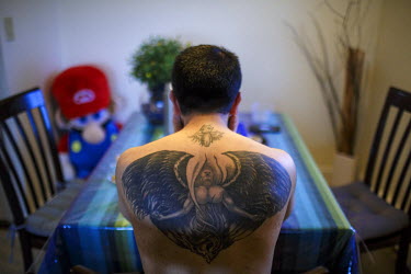 An Iranian Bahai refugee sitting at his dining table, showing his tattoo, which he got in India.