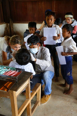 Spanish and Cambodian dentists examine a child's teeth during an outreach session in a school.