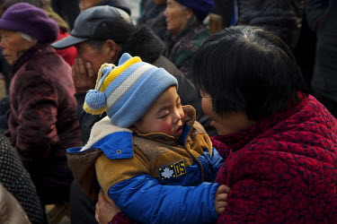 An elderly woman with a child among a crowd of villagers gathered for Chinese New Year celebrations.  The elderly tend to take care of the children while the working generation earn the family's livin...