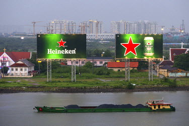 During a heavy monsoon rain storm, a coal barge passes two huge advertisements for Heineken beer on the Saigon River.