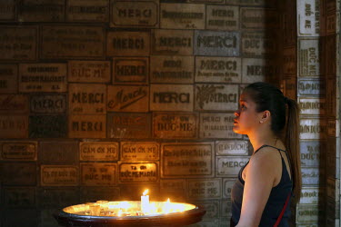 A woman stands beside a tray of burning votive candles in the Notre-Dame Cathedral Basilica of Saigon.