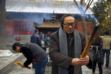 Traditional storyteller Master Li prays, incense in hand, in a temple.