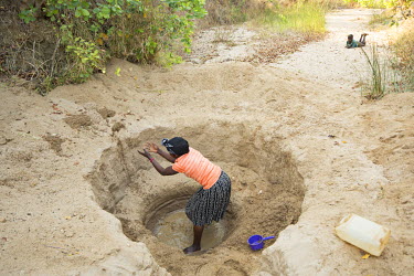 Isabel Mvula (34) digs out a hole in a dry river bed in order to find a source of water.