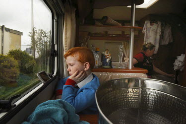 Irish Traveller Dennis Sheridan (7) watches a video on his iPhone in the family trailer on a rented site in Essex.