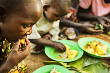 Moses (10) and his sisters eat a meal of matoke, a staple made from green banana, dried silver fish and greens from from their mother, Gertrude Ndolikye's garden.