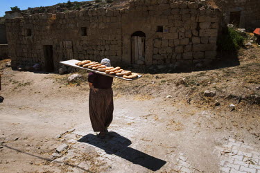 A woman carries a wooden board on her shoulder laden with freshly baked loaves of flat bread.