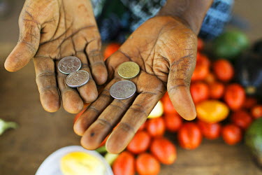 Molly Nanyomo (52) holds some coins as she serves customers at her roadside stall from where she sells fruits and vegetables.