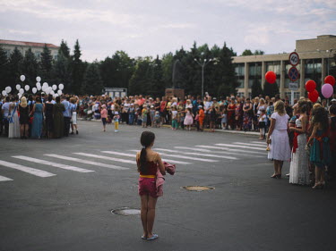 A young girl stands apart from a crowd celebrating the end of the school year.