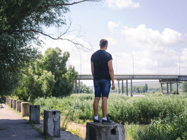 Alexander stands on a bollard and stares towards a bridge that crosses the Dniester River.