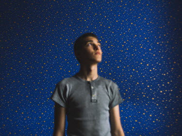 Nikita stands in his room with wallpaper is decorated with stars.