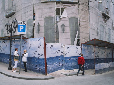 People walking past a hoarding, shielding a building being restored.