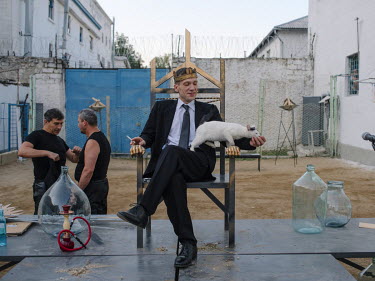 Mihai, a prisoner serving a life sentence at Penitentiary Nr. 17, wears a crown while smoking a cigarette and stroking a cat, seated on a throne on the stage of a production of Hamlet inside the priso...